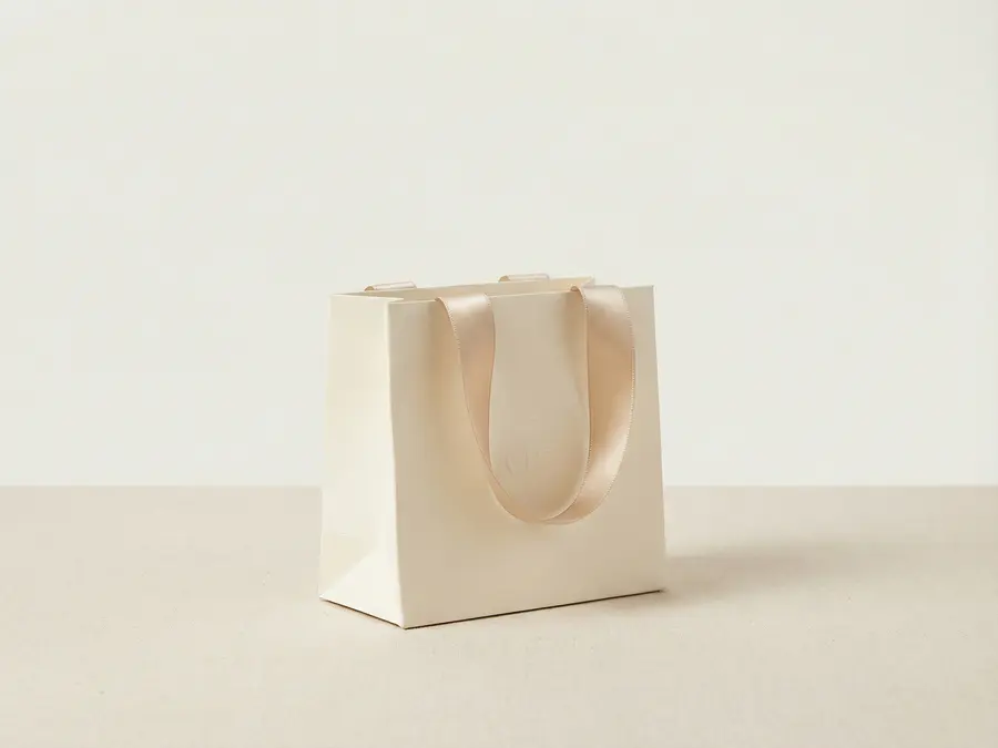 Small luxury boutique paper bag with satin ribbon handles for cosmetics brand packaging.